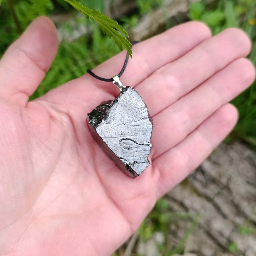 Glaenzender Anhaenger aus Edelschungit in der Hand liegend.