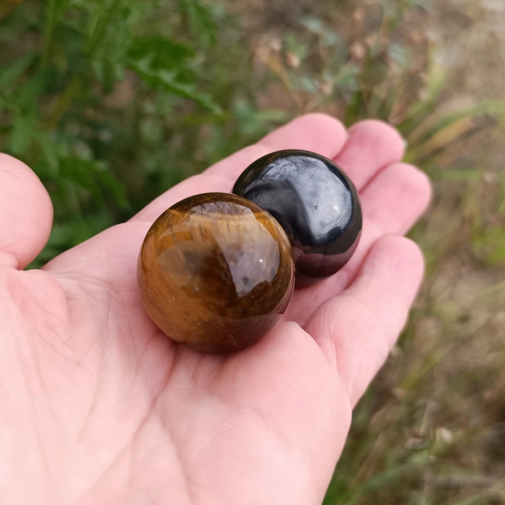 Zwei Kugeln aus Tigerauge und Schungit in der Hand haltend