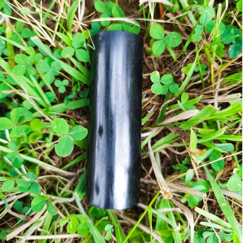 Schungit-Zylinderstab poliert, glänzend schwarz, auf Naturuntergrund liegend