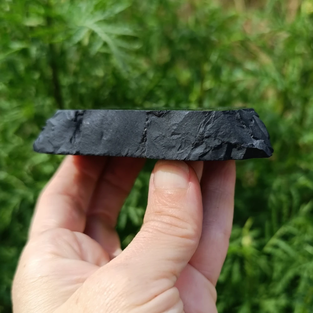 Schungit-Platte mit Naturkante, unbearbeiteter Rand, in der Hand gehalten