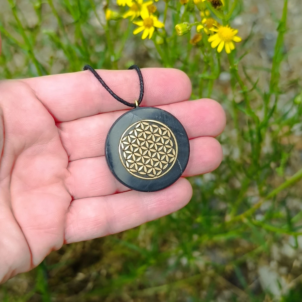 Runde Schungitkette mit goldfarbenen Lebensblume in der Hand liegend