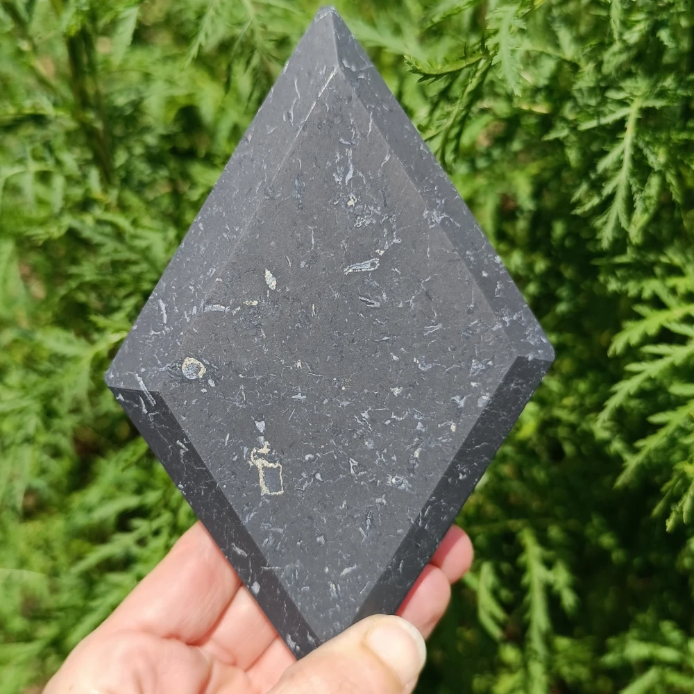 Schungit-Raute, unpoliert, dunkelgrau, in der Hand gehalten, Naturhintergrund