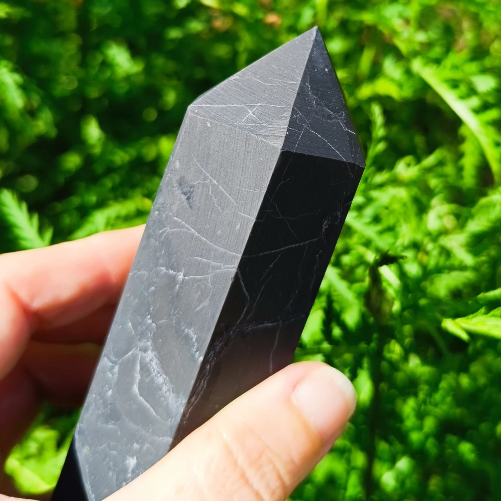 Schungit-Obelisk, poliert, in der Hand gehalten, Naturhintergrund