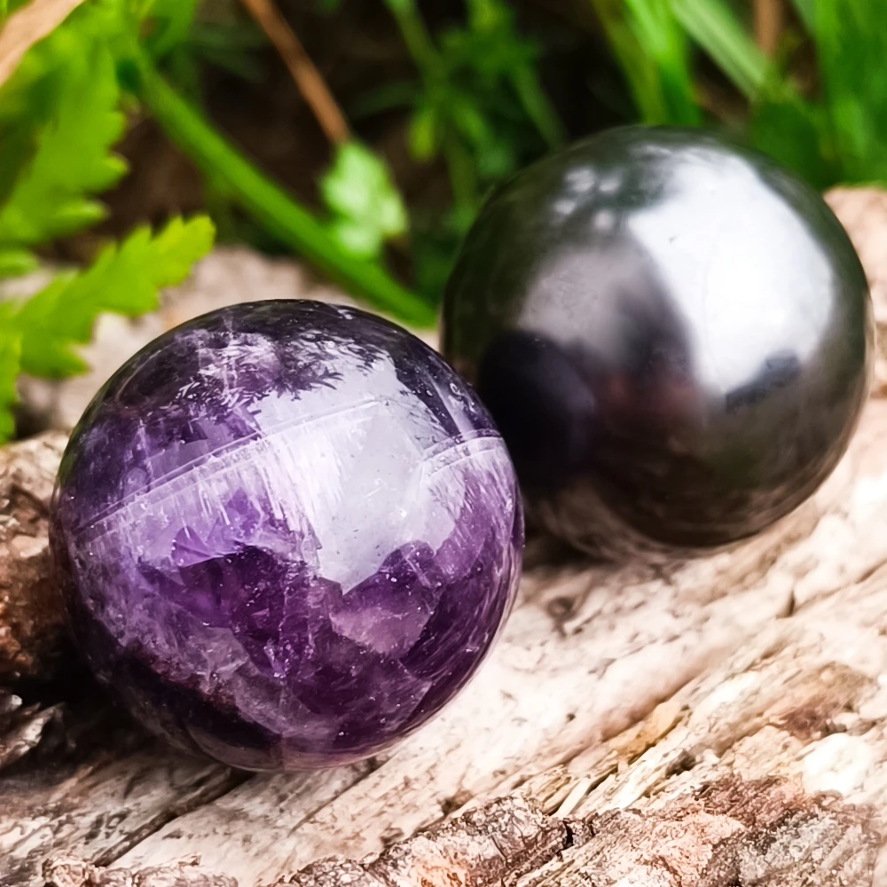 Zwei Kugeln aus dunklem Amethyst und Schungit auf Holz