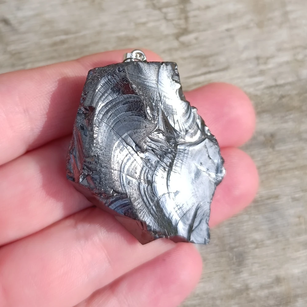 Elite-Schungit Schmuckanhänger, silbrig-metallische Rohstruktur in der Hand