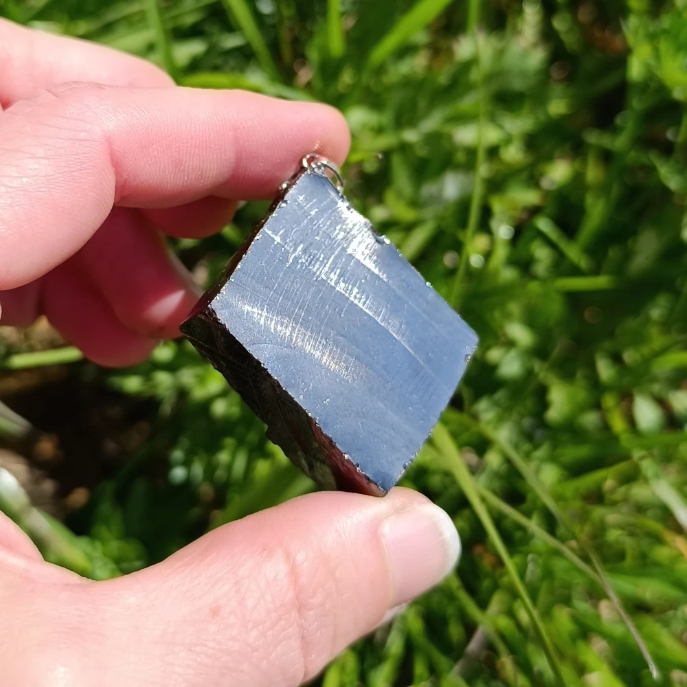 Edelschungit-Kettenanhenger am Baumstamm.