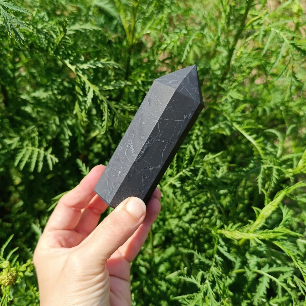Schungit-Obelisk, poliert, in der Hand gehalten, Naturhintergrund