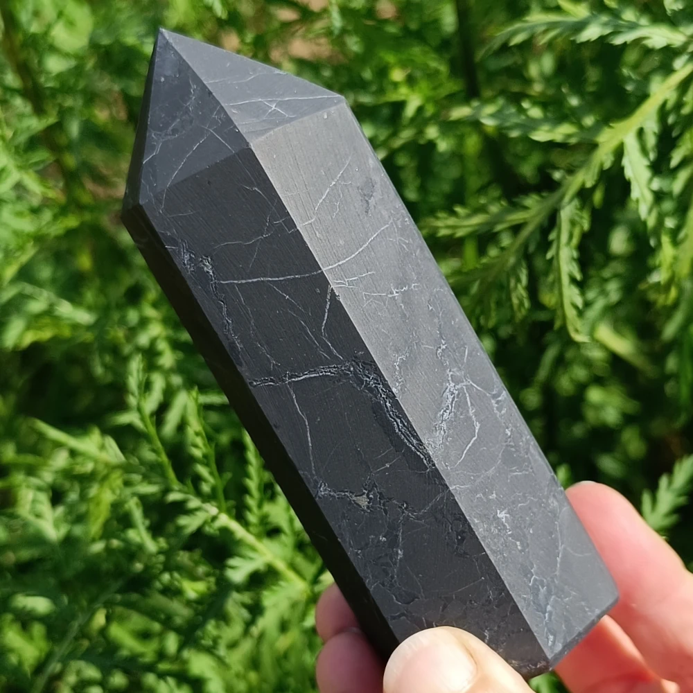 Massiver Schungit-Obelisk, unpoliert, in der Hand gehalten, Naturhintergrund