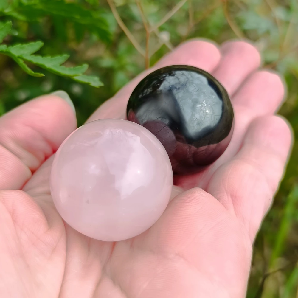 In der Hand haltens zwei Kugel aus Schungit und Rosenquarz
