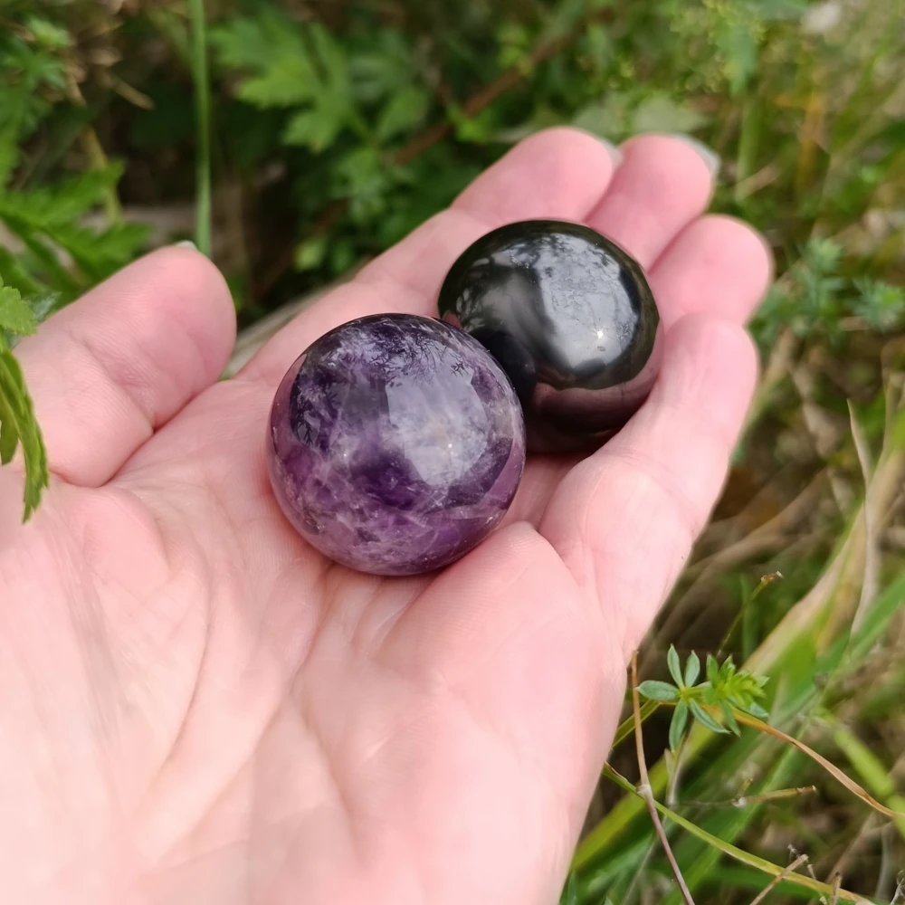 Kugeln aus Schungit und Amethyst in der Hand haltend