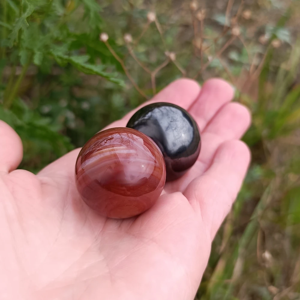 Zwei kleine Kugeln in der Hand aus Schungit und Karneol