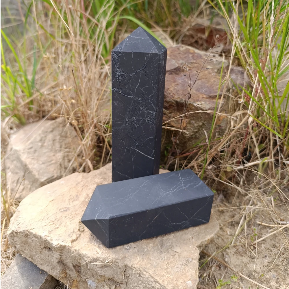 Schungit-Turm, unpoliert, auf Steinuntergrund stehend, Naturhintergrund