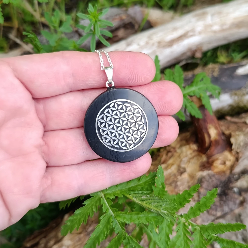 Runde Schungitkette mit silberfarbenen Lebensblume in der Hand liegend