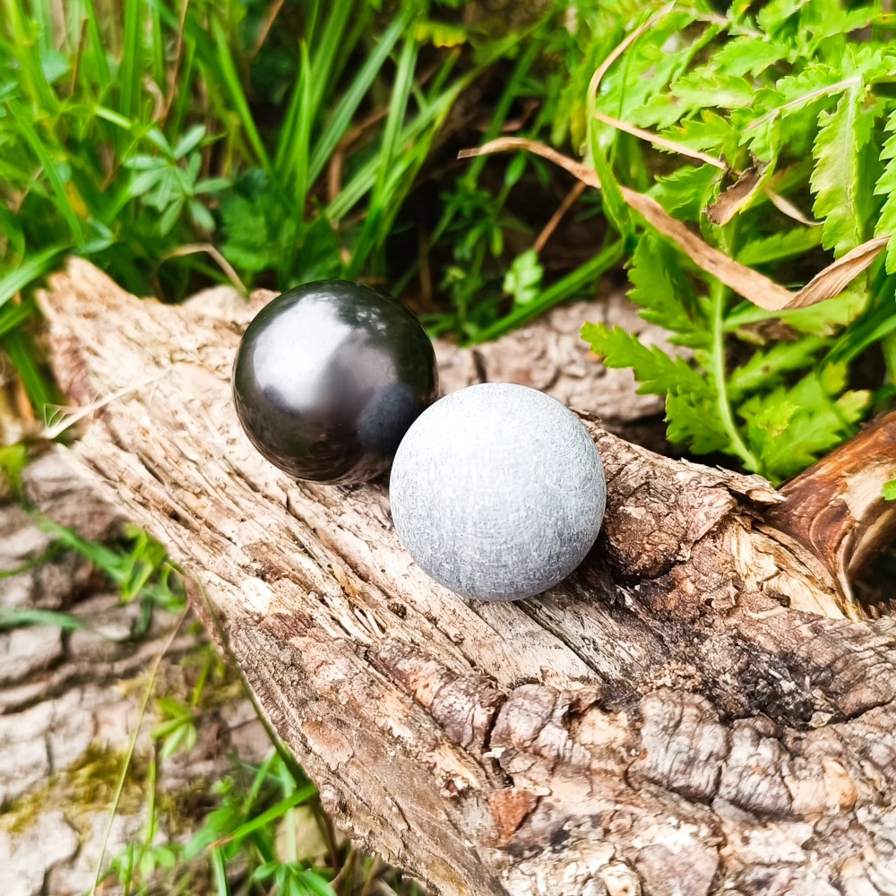 Zwei Kugeln liegend auf Holzstamm aus Schungit und Talkchlorit