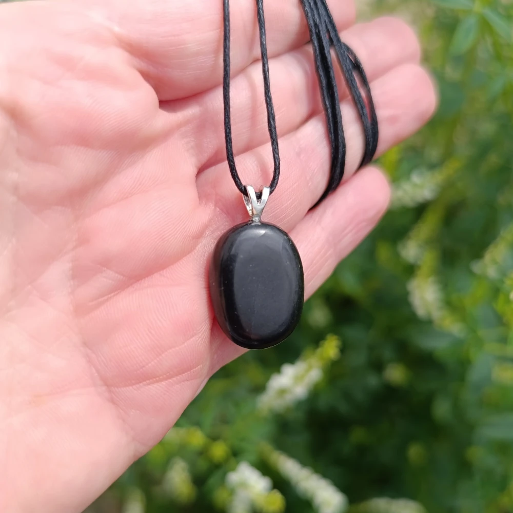 Schungit Anhänger in der Hand bei Sonnenstrahlen