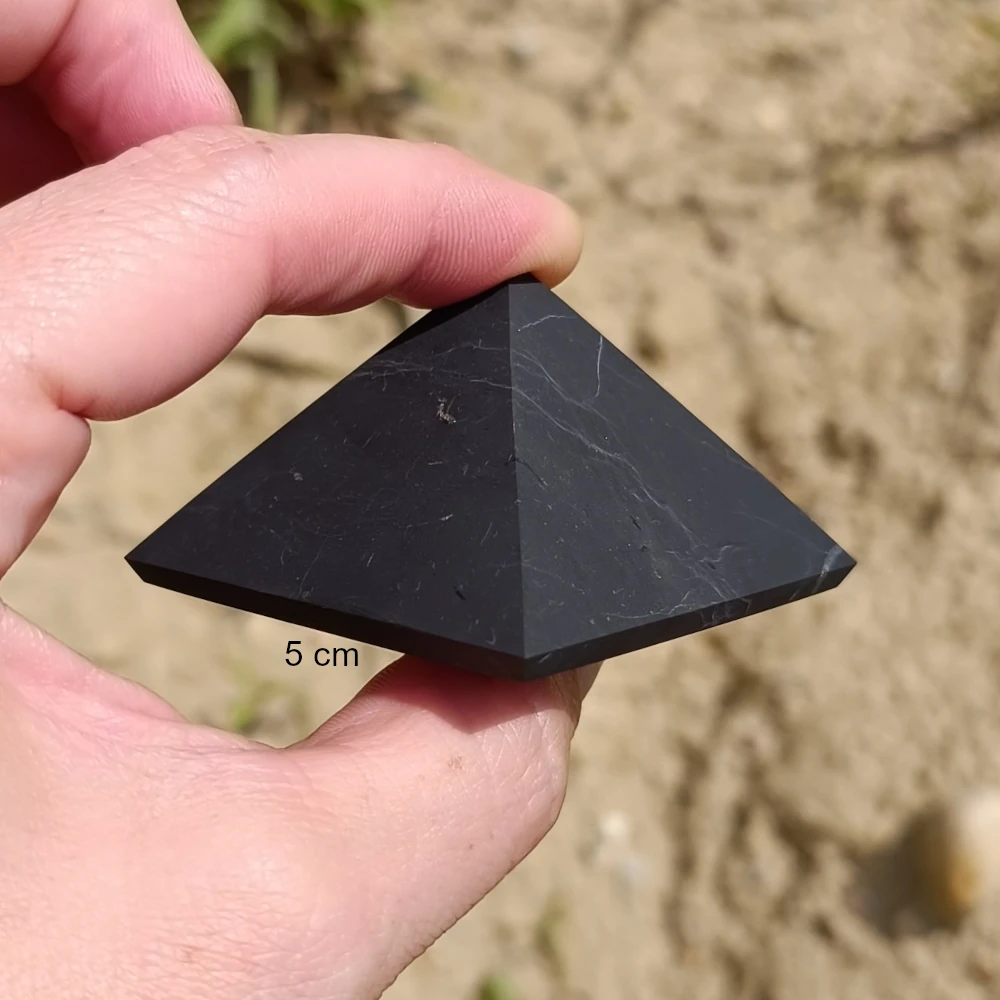 Unpolierte Pyramide aus Schungit zwischen zwei Fingern