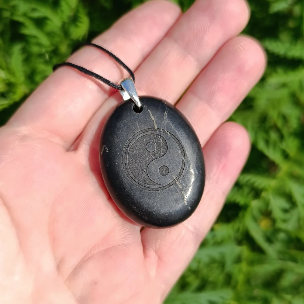 Schungit-Anhaenger mit dem Symbol Yin und Yang in der Hand
