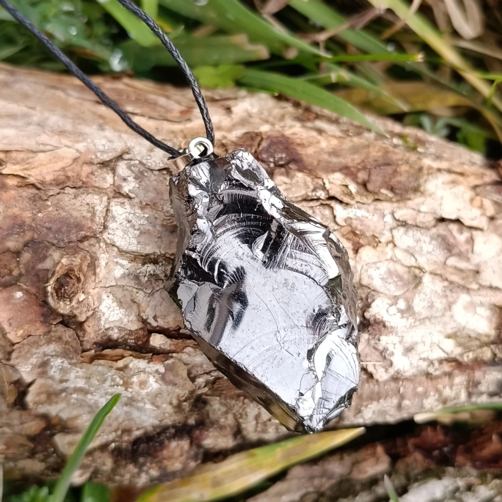 Glaenzender Halsanhaenger aus Edel-Schungit auf Holzstamm liegend.