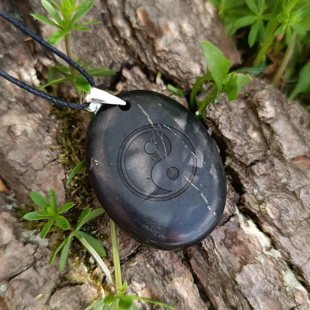 Schungit-Anhaenger mit dem Symbol Yin und Yang im Schatten liegend
