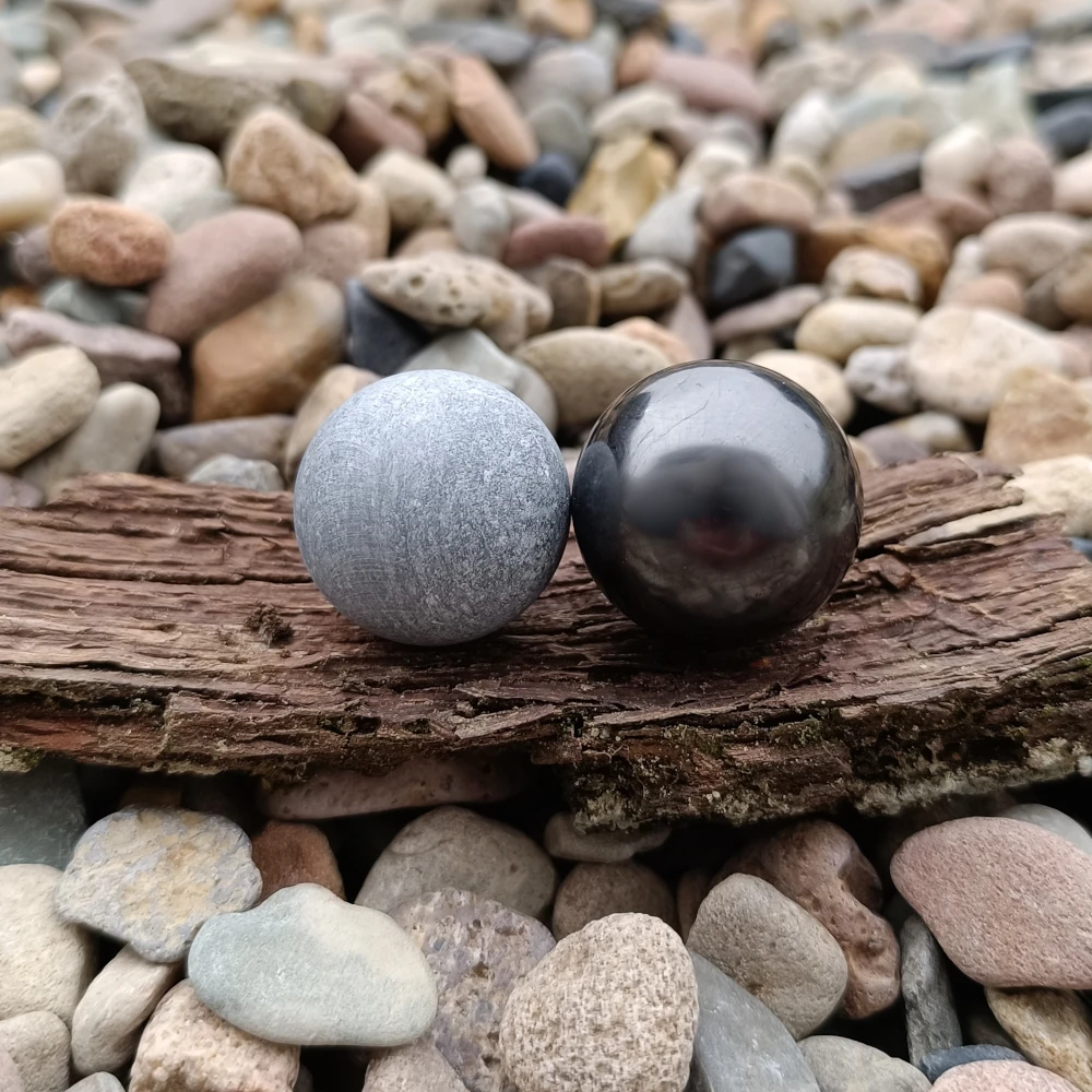 Zwei Kugeln aus Talkchlorit und Schungit auf Baumrinde