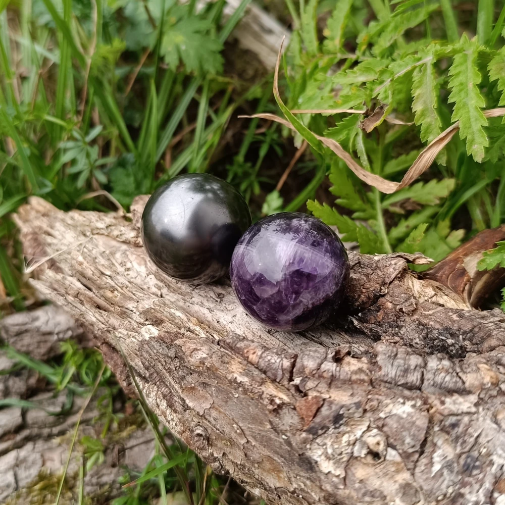 Zwei Kugeln aus Schungit und Amethyst auf Baumstamm