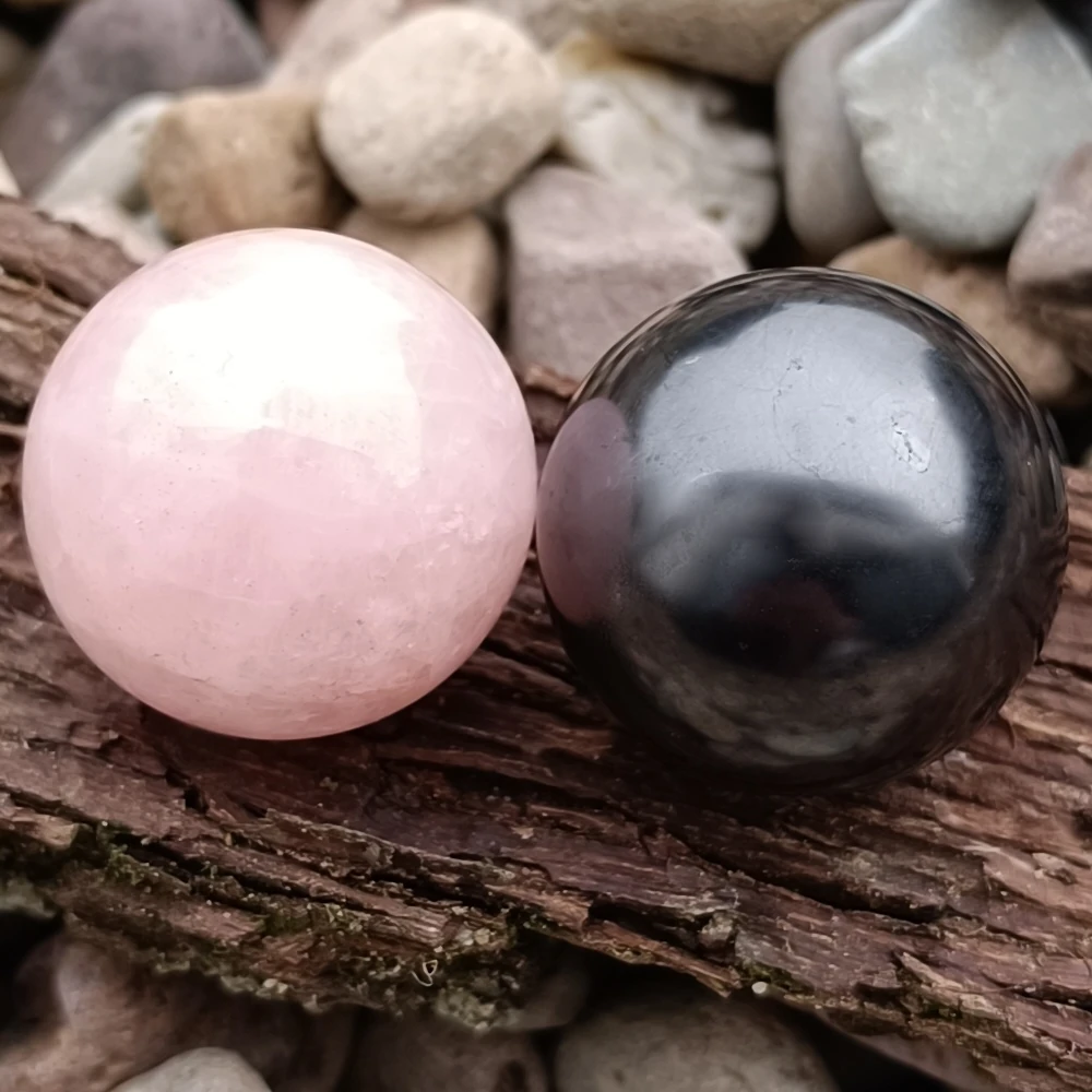 Zwei Kugel aus Rosenquarz und Schungit auf Baumrinde liegend
