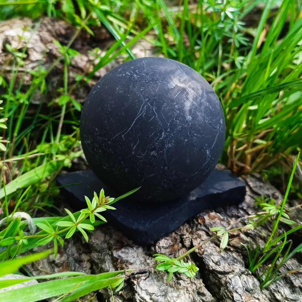 Schungit Kugel und Halter unpoliert auf Holzrinde stehend