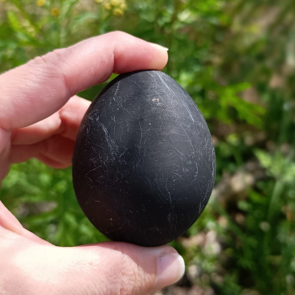 Schwarzes Schungit Ei zweischen zwei Fingern gehalten
