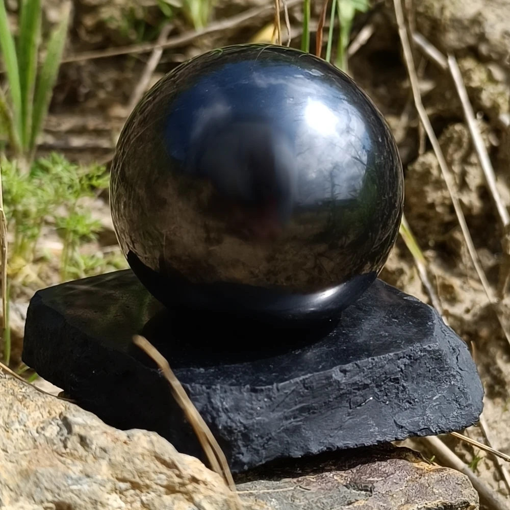 Schwarze Schungit Kugel mit Untersetzer im Sand stehend
