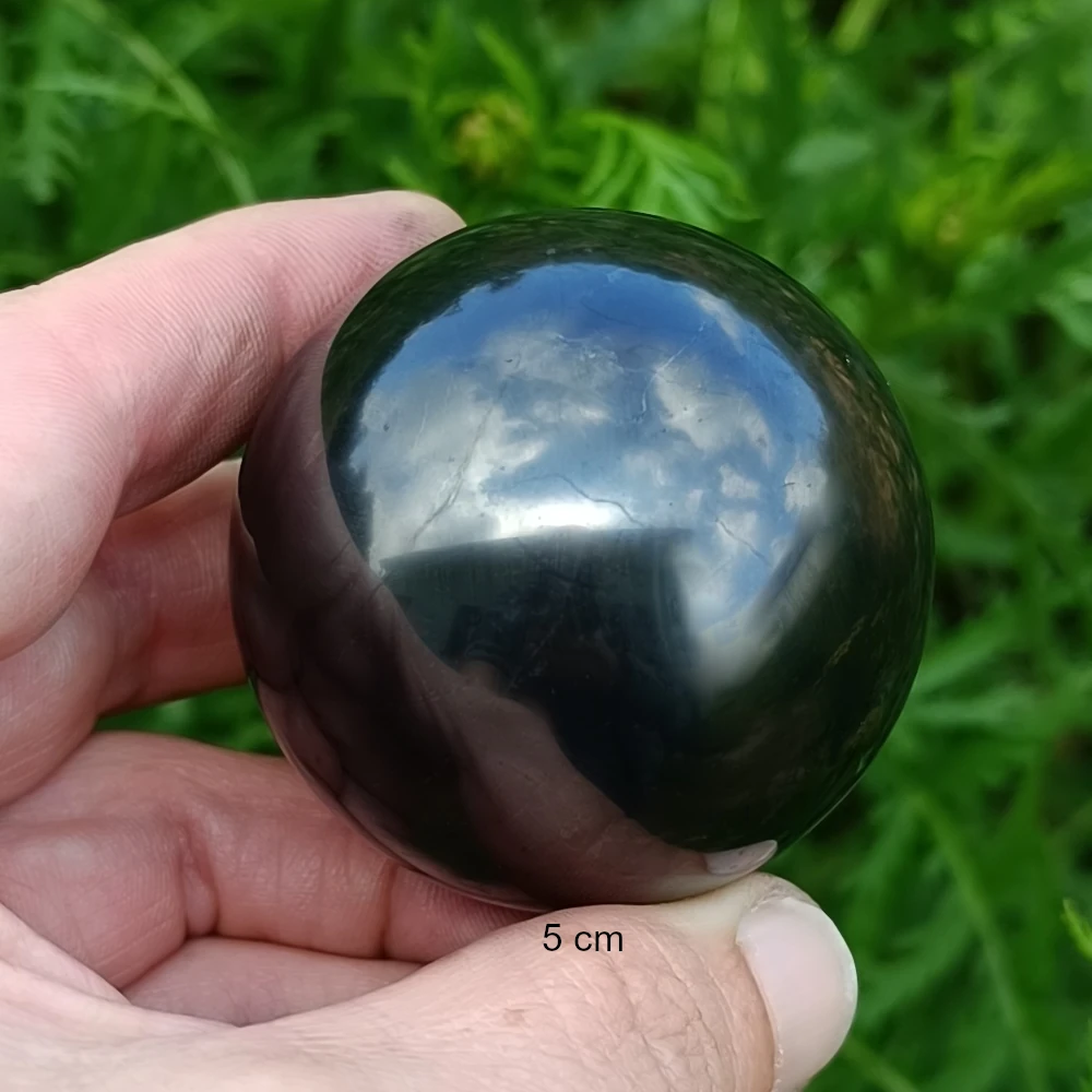 Schungit Kugel fuenf Zentimeter in zwei Fingern haltend
